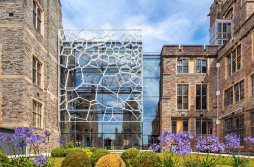 The University of Bristol Fry building with the designed glass front on the left hand side adjoining the older building on the right, with flowers in the foreground